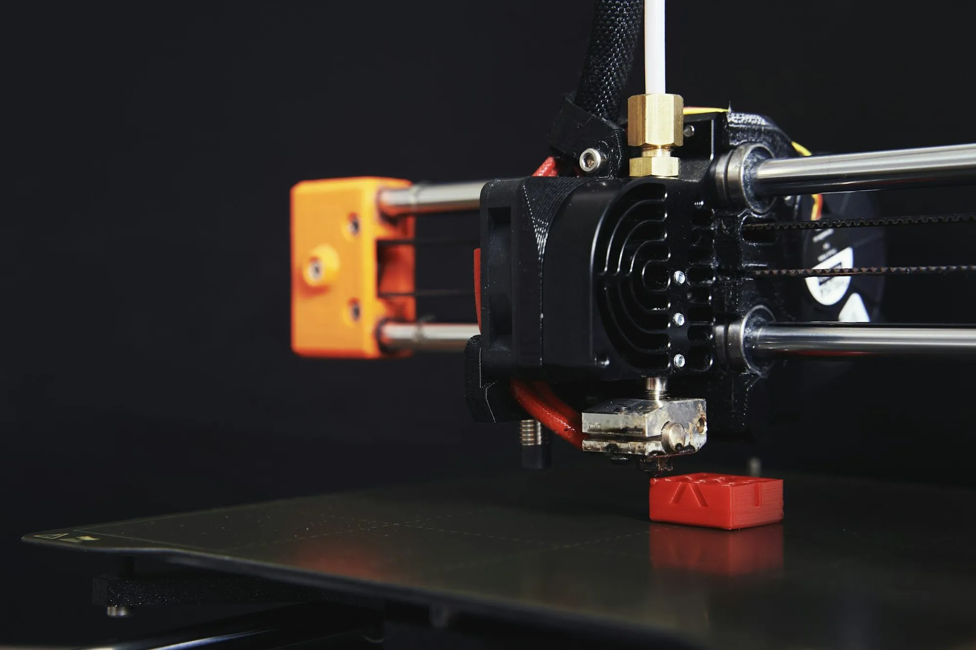 Druckkopf eines 3D-Druckers über einem gedruckten roten Bauteil vor dunklem Hintergrund