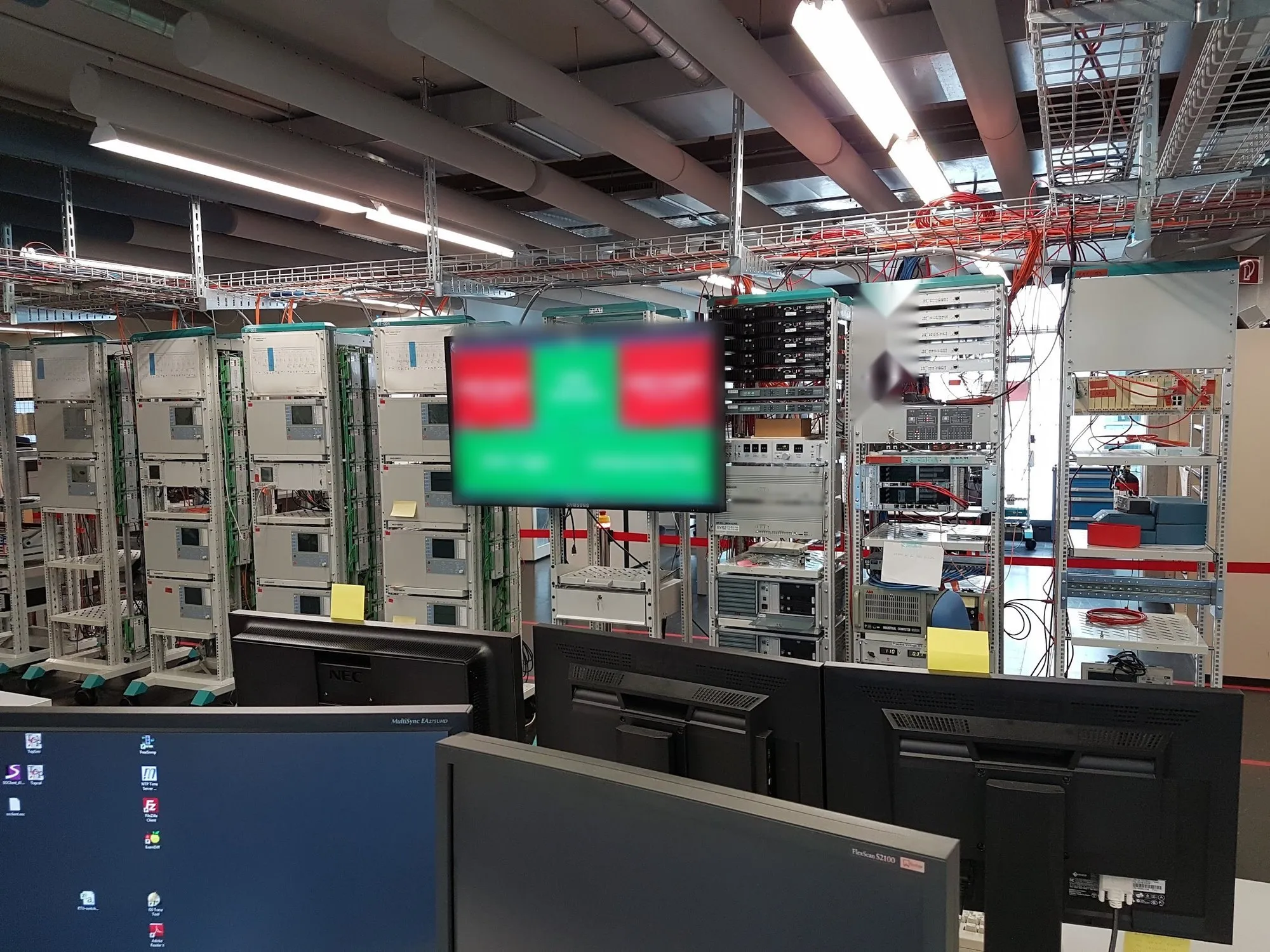 Test laboratory with racks of protection and control devices and a screen showing the build status of automated tests